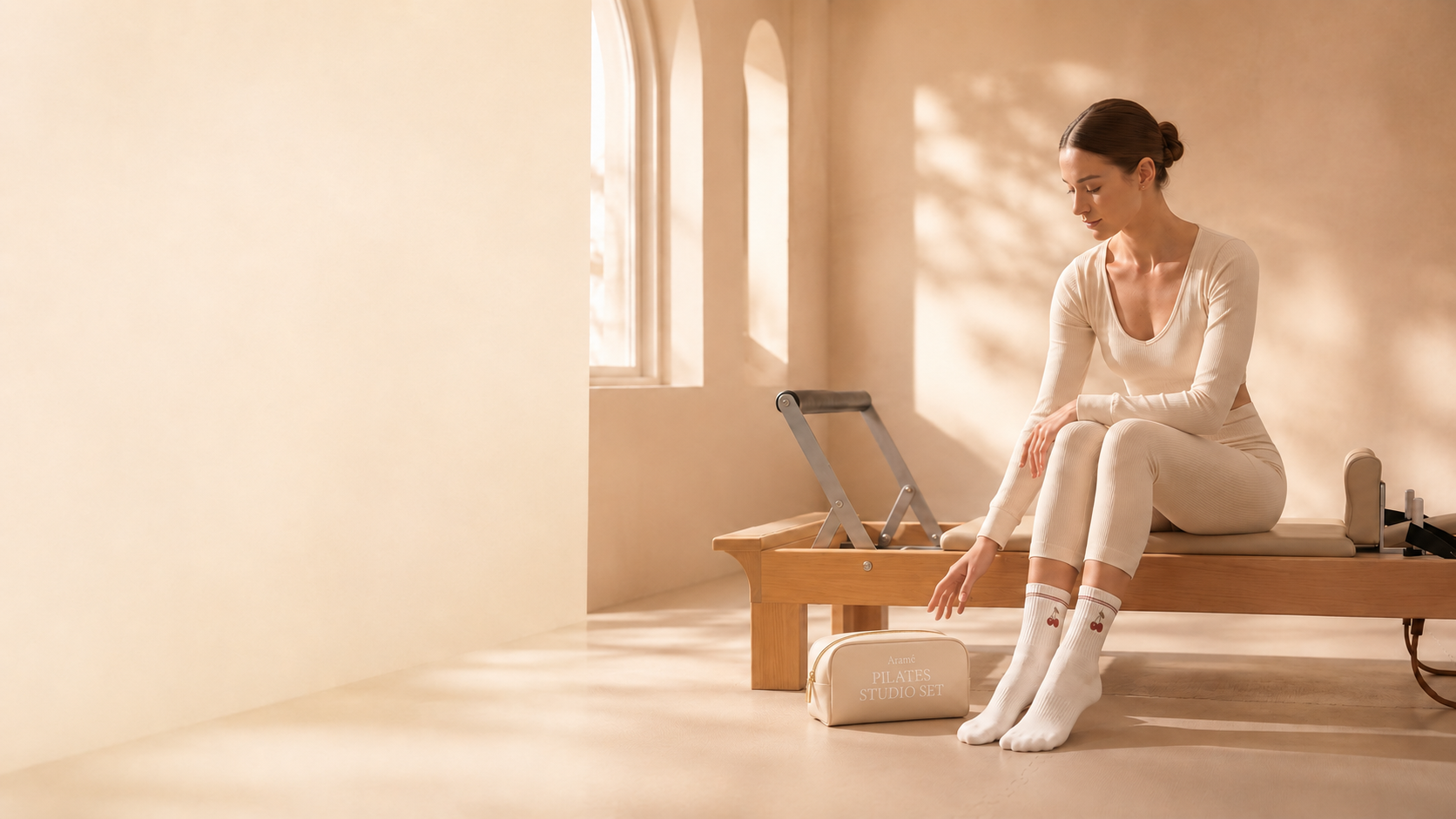 Soft cream Aramé Pilates Studio Set bag beside a model on a reformer